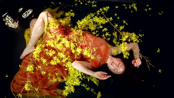 Enigmatic Woman is Lying in Water with Flowers in River or Lake Shallow Top View on Sexy Female Body