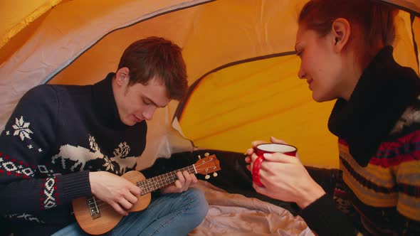 Woman in Tent Holds Mug of Hot Tea and Listens to Man Playing a Ukulele