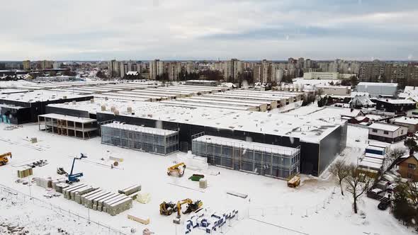 Logistics building under construction with Kaunas city residential district behind during snowfall,