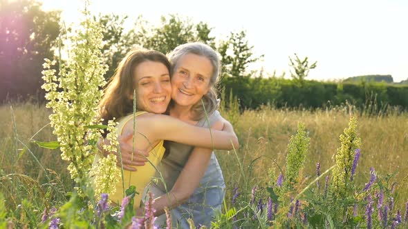 Senior Mother with Gray Hair with Her Adult Daughter Looking at the Camera in the Garden and Hugging