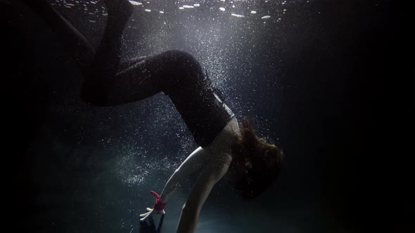A Woman in a Suit Is Swimming Underwater Doing a Somersault in the Water Her Long Hair Flying