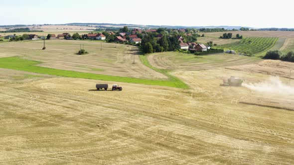 Aerial Drone Shot  a Combine Harvester and a Tractor in a Field in a Rural Area on a Sunny Day