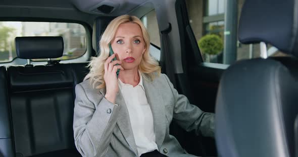 Mature Businesswoman Sitting in Back Seat of Car Talking on Mobile Phone.