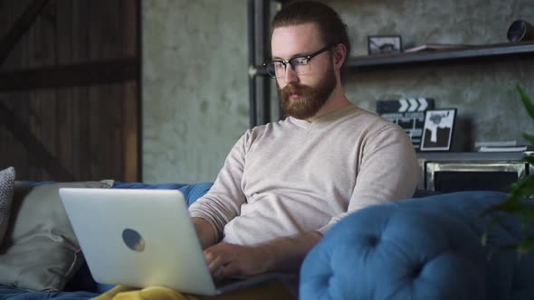 Young Bearded Businessman is Working on Online Project and Using Laptop at Apartment Spbd