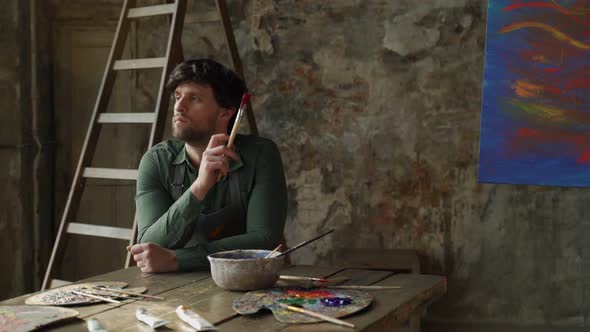 Tired Man in an Art Studio Sits on a Chair After Painting an Abstract Painting