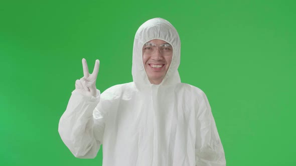 Male Wear Protective Uniform Ppe Smiling To Camera With A Victory Hand Sign In Green Screen Studio