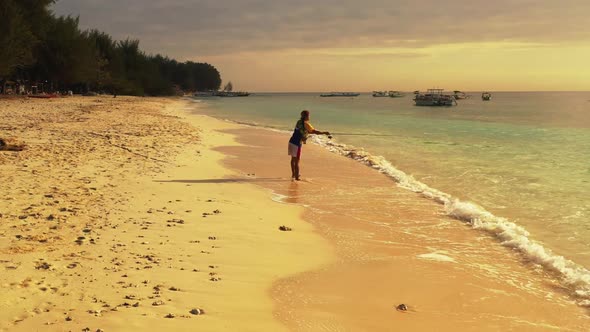 Boy fishing on tranquil lagoon beach wildlife by turquoise ocean and white sandy background of Lombo