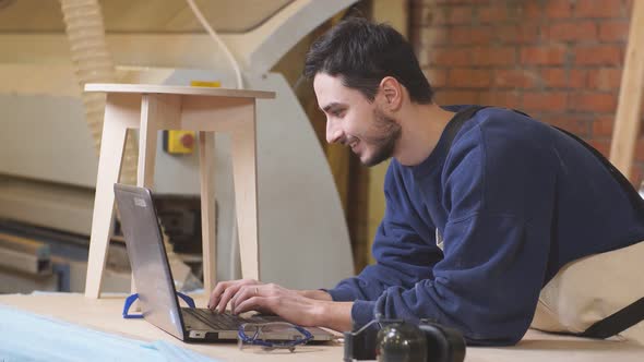 Furniture Maker Skillfully Make a Wooden Chair on Workbench and Use Laptop