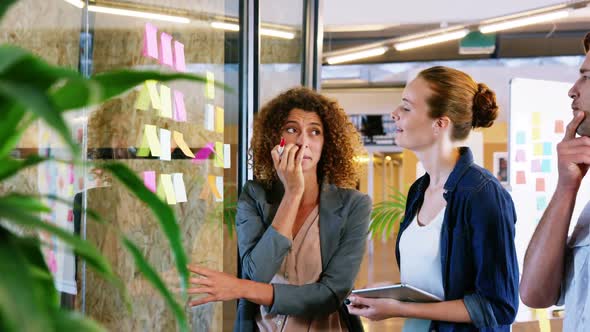 Woman writing on sticky note and discussing with colleagues