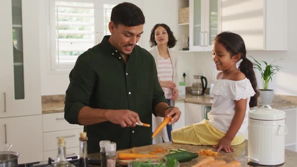 Hispanic father teaching daughter sitting on countertop cooking