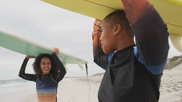 Happy african american female friends on the beach holding surfboards