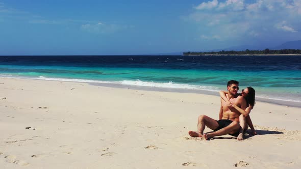 Young couple in swimsuit with slim bodies tanning on quiet exotic beach by the blue turquoise sea on