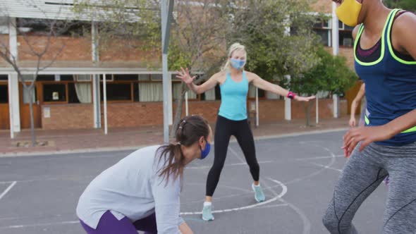 Diverse female basketball team wearing face masks playing match, scoring goal