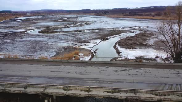 Gloomy scene of nature. Polluted river floating under the bridge on muddy background in springtime. 