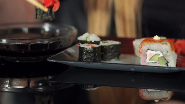 Woman Eating Sushi with Chopsticks on Black Table