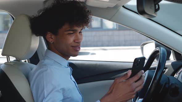 Young Business Guy of Ethnicity Scrolls the News Feed on the Smartphone While Sitting in the Car