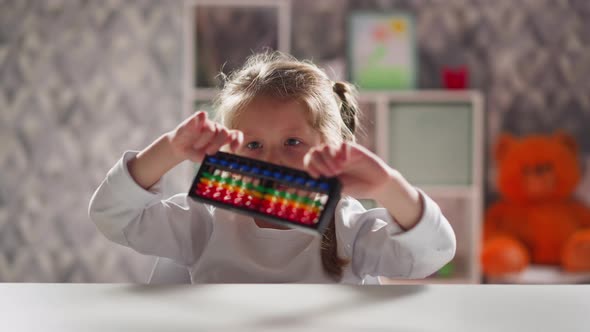 Curious Girl Turns and Looks at Abacus Sitting at Table