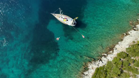 Aerial view of two women floating on inflatable next to sailing boat, Greece.