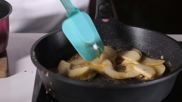 cook prepares fruit. ripe chopped pear is fried in frying pan. Filling for pie