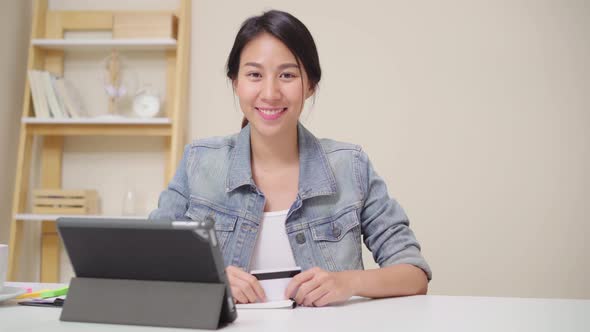 Asian woman using tablet buying online shopping by credit card while wear casual sitting on desk.