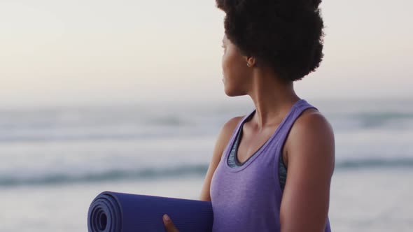 Portrait of happy african american woman with yoga mat on sunny beach
