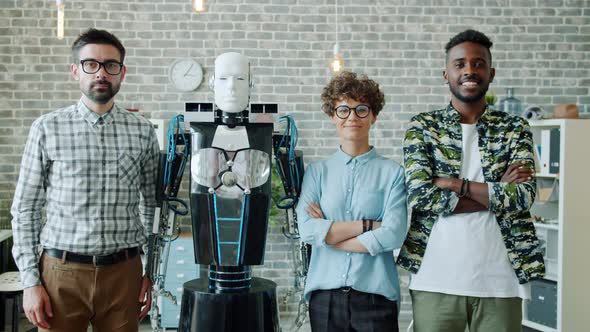 Portrait of Smiling Engineers and Robot Looking at Camera Standing in Office