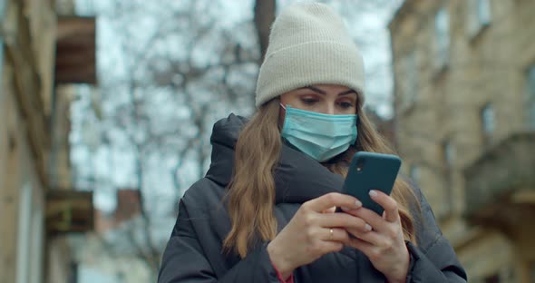 Portrait of Woman in Medical Protective Mask Typing By Mobile Phone Outdoors. Close Up Cheerful Girl