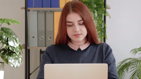 Young professional red hair female student using computer sitting at office desk.