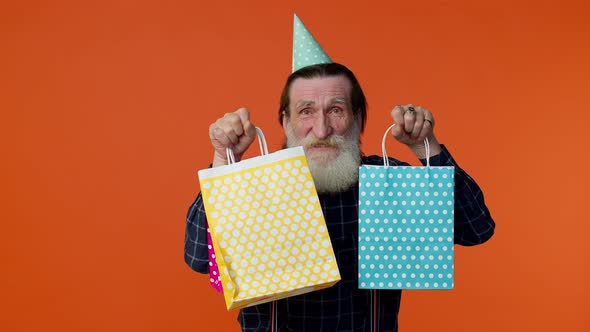 Elderly Bearded Man Showing Shopping Bags Advertising Discounts Looking Amazed with Low Prices