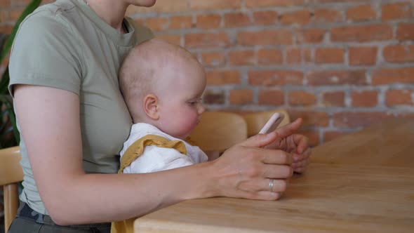 Cute Caucasian Baby Playing on the Smartphone While Sitting on Her Moms Lap. Technology and Kids