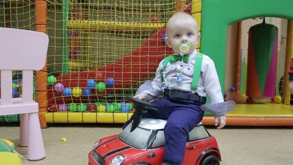 Little Boy in a White Shirt in a Red Toy Car at Home