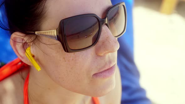 Portrait, a Young Woman in Sunglasses and Bluetooth Earphones Is Watching Video From Smartphone