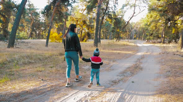 Young Mother Walking with a Little Son in Autumn Park. Happy Family in Autumn Park.