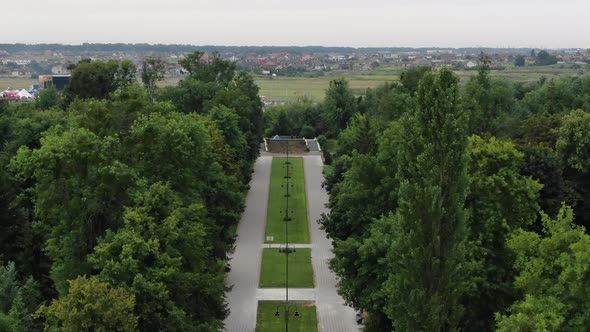 Aerial View of Sidewalk Going Through Park Surrounded by Trees Leading to Packed Field of Tents at a