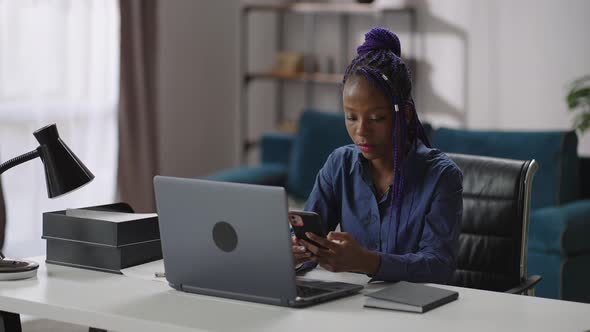 Young Afroamerican Businesswoman is Using Smartphone in Working Place in Her Office Sitting at Table