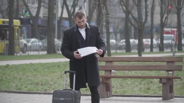 Dissatisfied Caucasian Man Folding Map and Shaking Head As Standing on Alley in Park