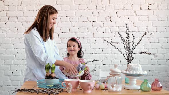 Young Woman and Child is Setting Easter Festive Table with Bunny and Eggs Decoration Wreath