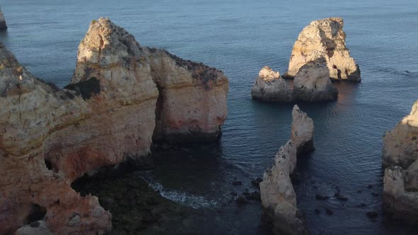 Golden limestone sea cliffs and rock stacks along Portuguese coast near Lagos, high angle.