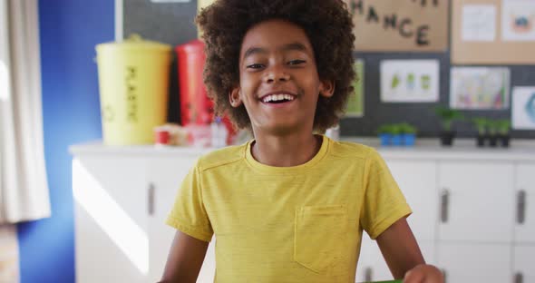 African american schoolboy standing, smiling in classroom looking at camera learning about recycling