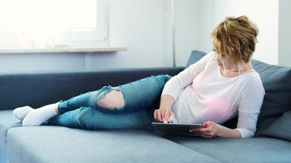 Woman is Lying on the Couch with a Tablet