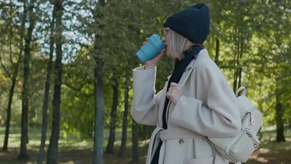 Girl Walks in the City Park on a Sunny Autumn Day Drinking From an Eco Cup