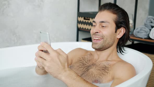 Cheerful Young Man Taking Bath and Using Smartphone Touching Screen at Home