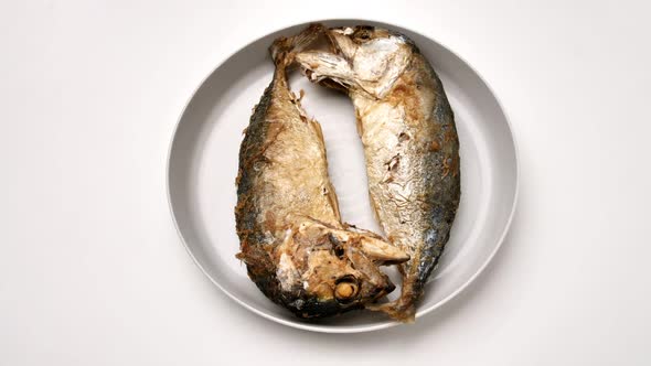 Top view of two fried mackerel on a white plate.