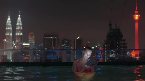 Woman with Pad in Rooftop Pool of Night Kuala Lumpur