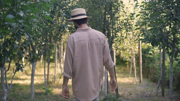 Back View of Young Happy Man Walking Outdoors in Garden Turning to Camera Smiling