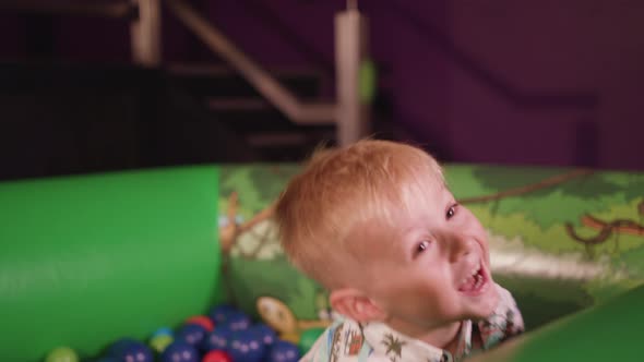 A Young Boy Plays in Ball Pit and Throws Balls Around whilst Smiling