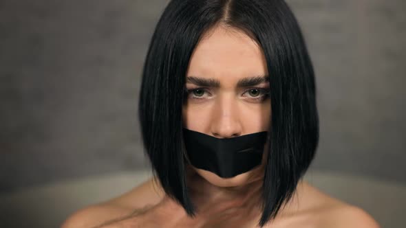 Serious Woman with Duct Tapered Mouth Grabbed By Male Hands Over Neck Looking at you