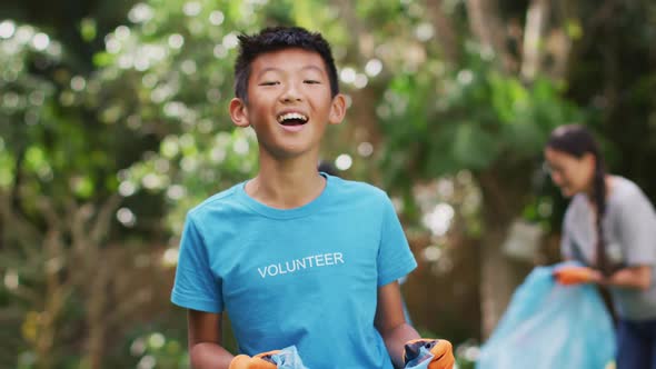 Laughing asian boy wearing volunteer t shirt holding refuse sack for collecting plastic waste