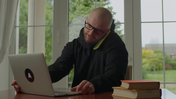 30s Man in Eye Glasses Talking on Mobile Phone Using Laptop