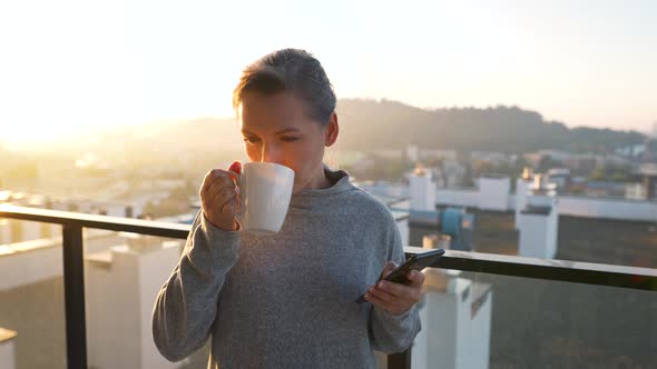 Woman Starts Her Day with a Cup of Tea or Coffee and Checking Emails in Her Smartphone on the